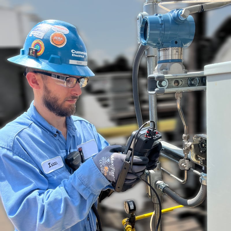 A man in a hard hat and glasses operates a device, focused on his task in a work environment