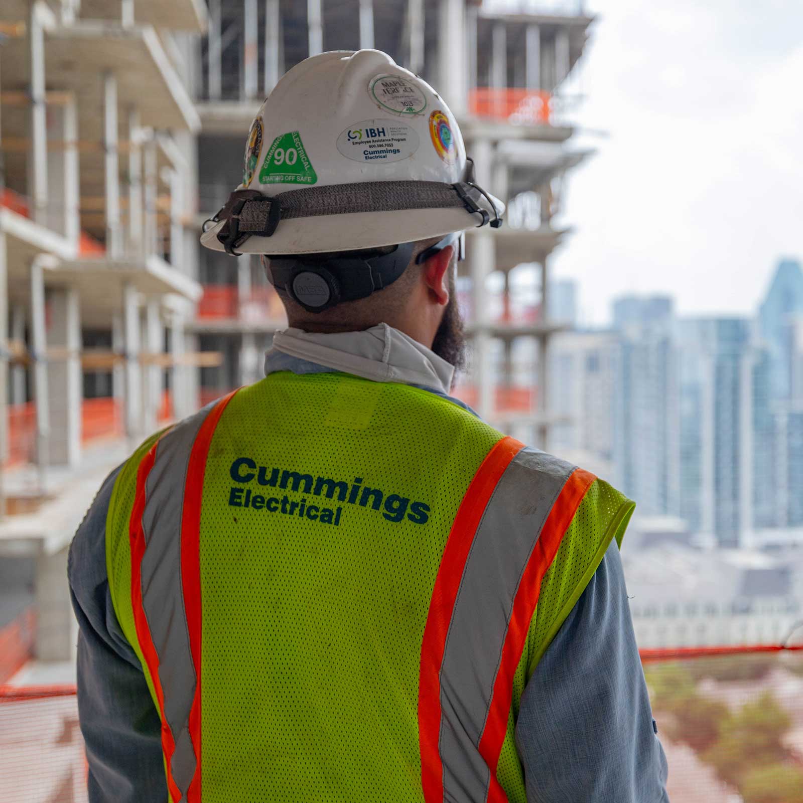 A construction worker in a hard hat and safety vest gazes over a city skyline, assessing the urban landscape