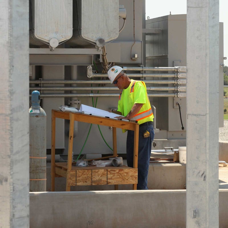A man stands on a wooden platform at a construction site, reviewing plans for the ongoing project