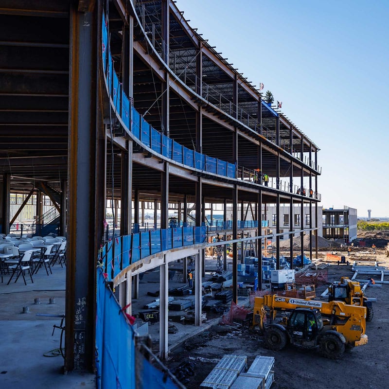 A multi-story steel-framed building under construction, with workers installing materials.