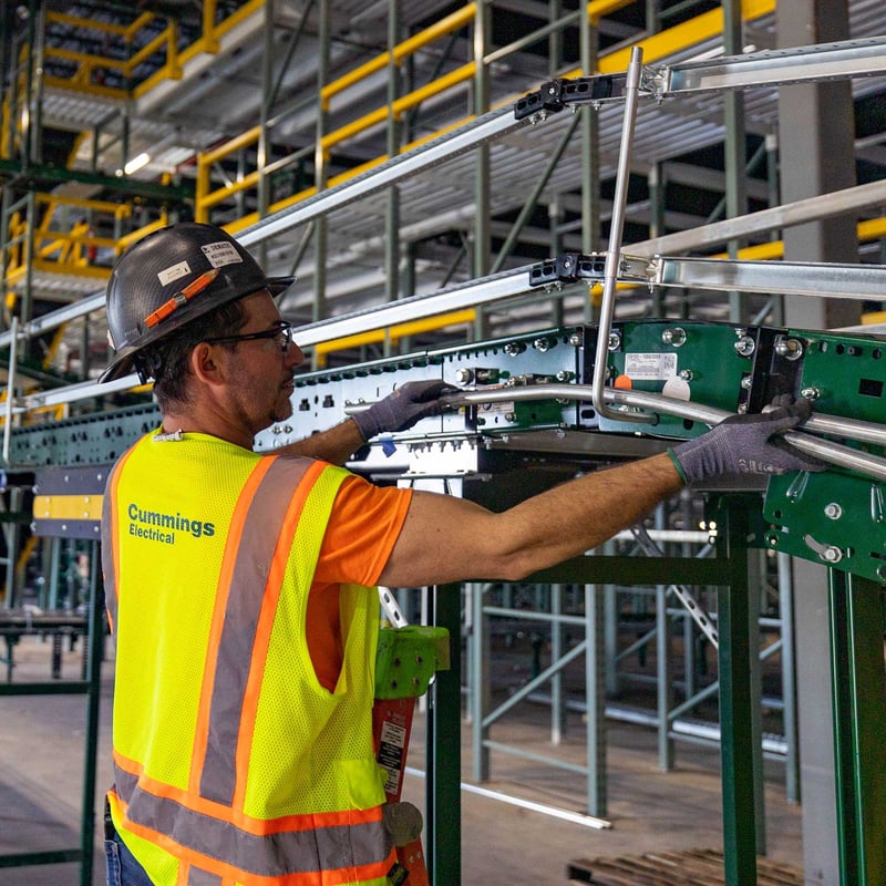 Electrician inspects machinery on a conveyor belt, ensuring proper function and safety in the workspace