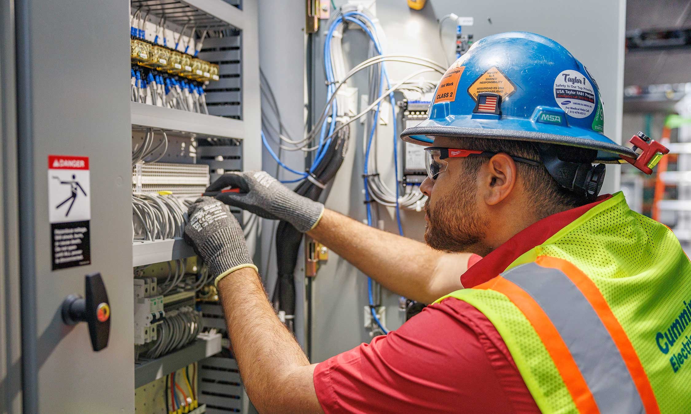 Electrician using a hard hat and a safety vest working on a panel