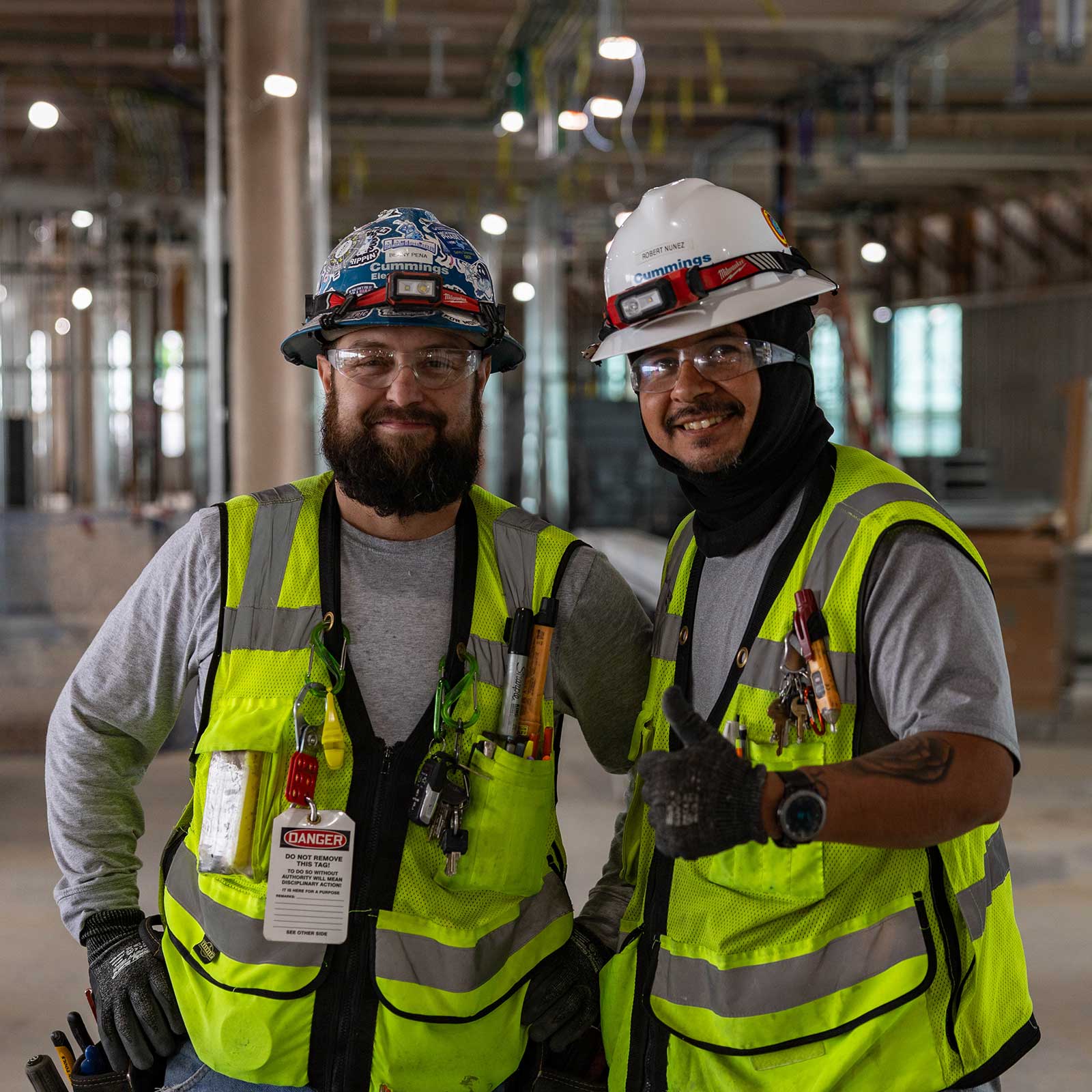 Two construction workers smiling for a photo in an unfinished building, showcasing teamwork and progress on the site