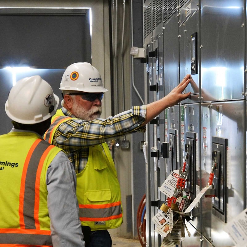 Two men wearing hard hats, standing side by side, engaged in a discussion