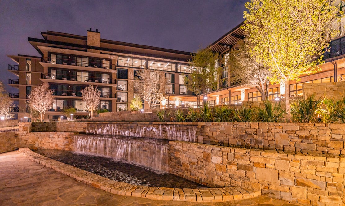 Nighttime view of a resort featuring terraced stonework, water features, and architectural lighting