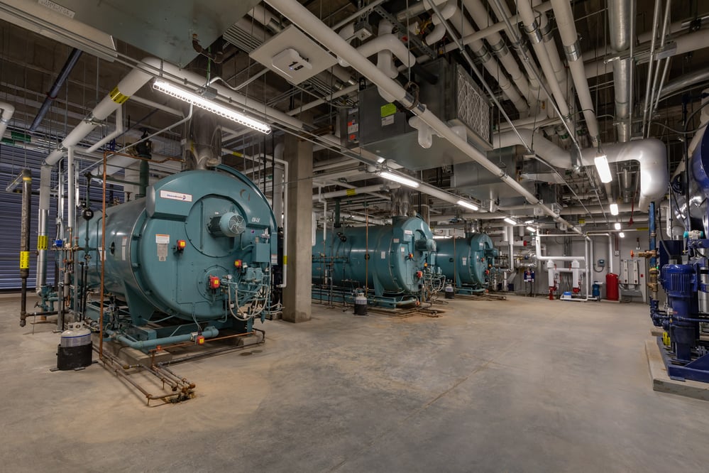 Large medical boiler room with various labeled piping and conduit