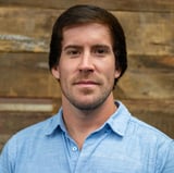 Headshot of Brandon Barajas wearing a button-down shirt, smiling in front of a wood background.