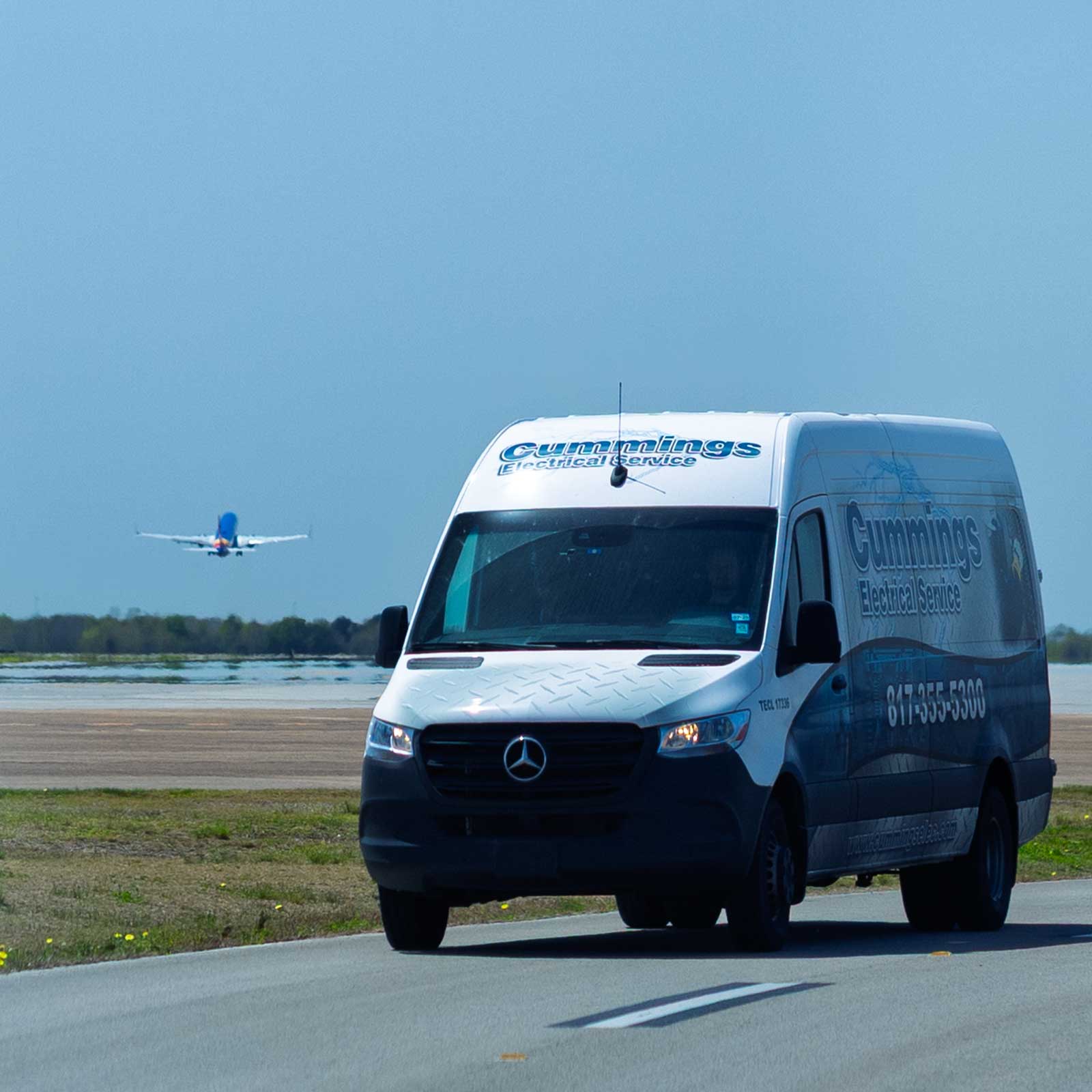 Cummings service van at airport with airplane taking off behind
