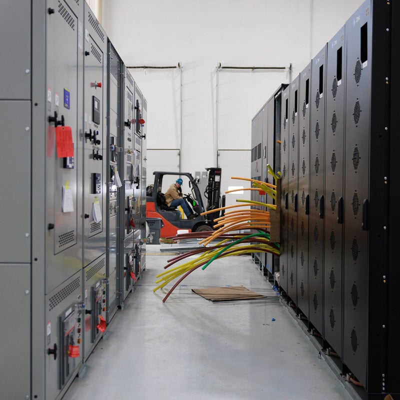 view of a row of panels with colorful conduits routed outside and a forklift in-between