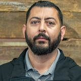 Headshot of Eder Morales wearing a polo shirt and black jacket, in front of a wood background.