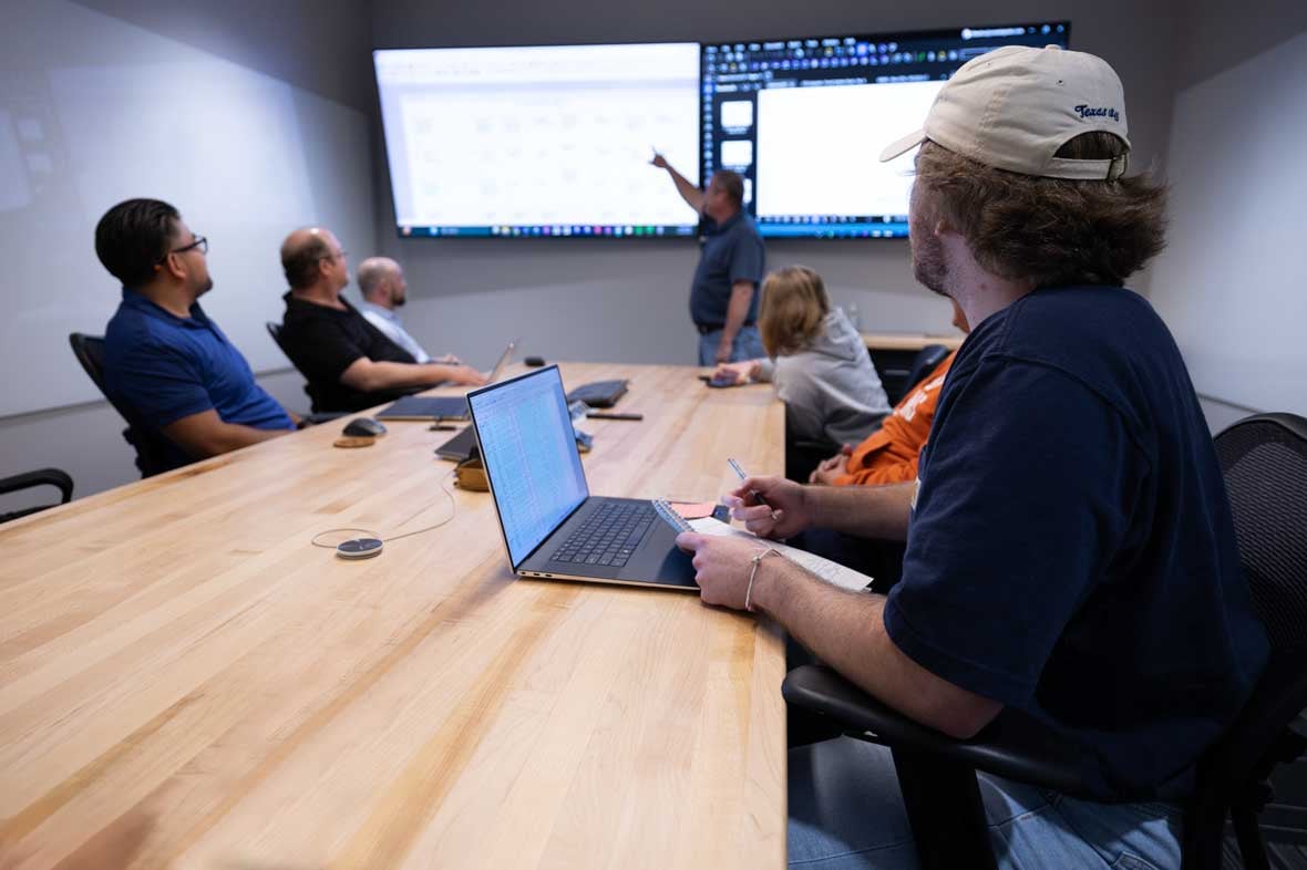 Engineering and design meeting with multiple men in room and one in the front pointing at a screen