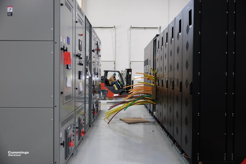 view of a row of panels with colorful conduits routed outside and a forklift in-between