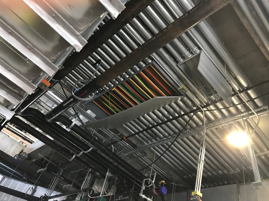 Ceiling view of multiple straight conduit with colorful wiring viewable through a panel opening