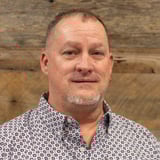 Headshot of James Chambers wearing a button-down shirt, smiling in front of a wood background.