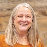 Headshot of Jill Gonzalez wearing an orange shirt, smiling in front of a wood background.