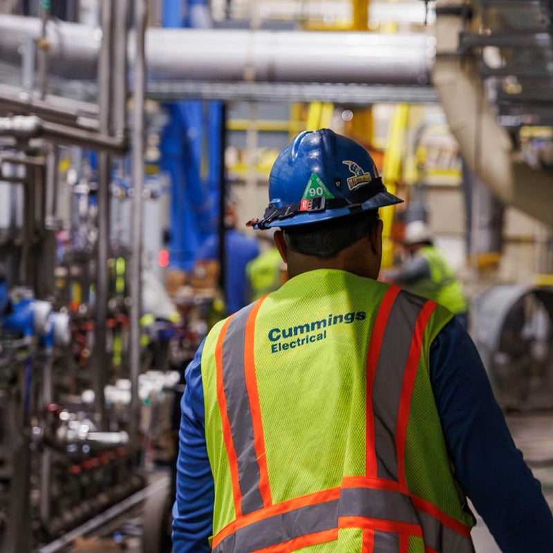 Cummings technician with PPE walking inside of a heavy industrial manufacturing facility