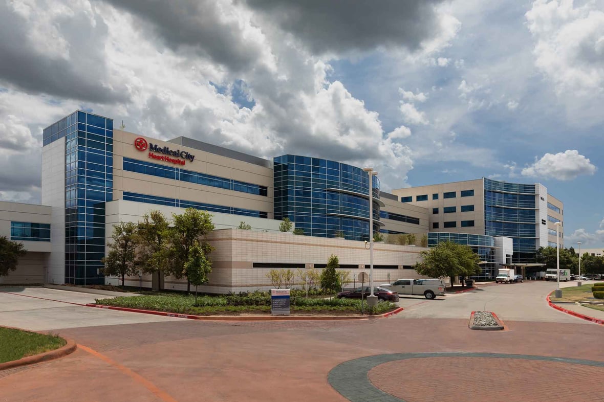 A hospital exterior view with cars parked outside and a cloudy sky