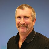 Headshot of Mark Harko wearing a polo shirt, smiling in front of a blue background.
