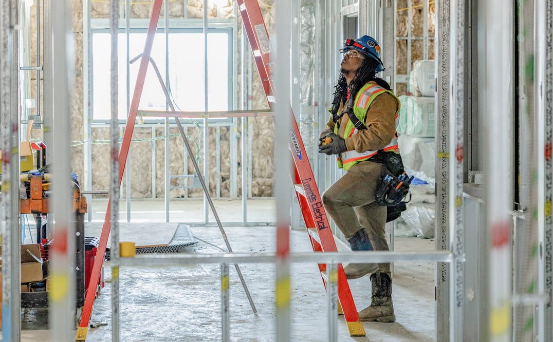 a man with PPE climbing a ladder in a room under construction