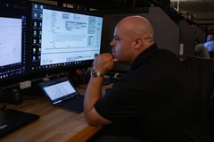 View of a man analyzing electrical drawings on a large monitor at a desk with a laptop open in front of him.