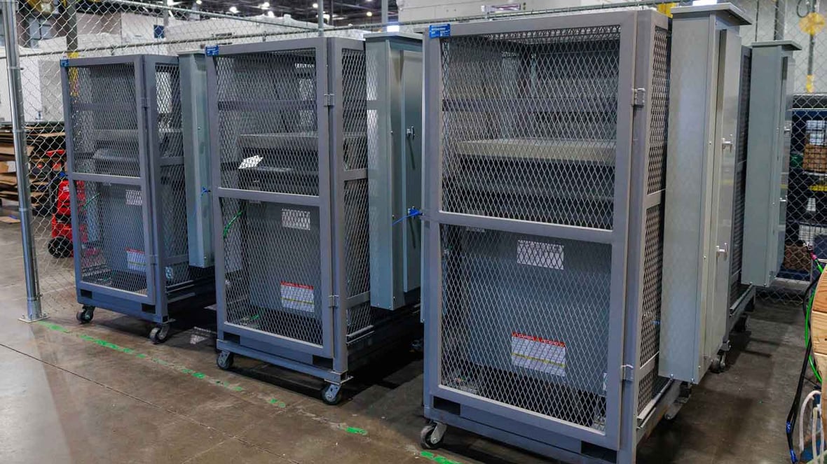 Row of electrical skids enclosed in metal mesh for secure transport and site use