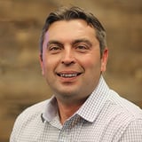 Headshot of Brad Samardzija wearing a button-down shirt, smiling in front of a wood background.