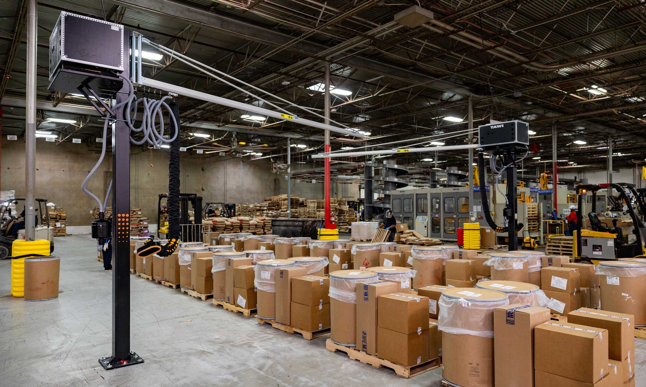 Interior of an active warehouse showing packaged goods, forklifts, and overhead power and data equipment